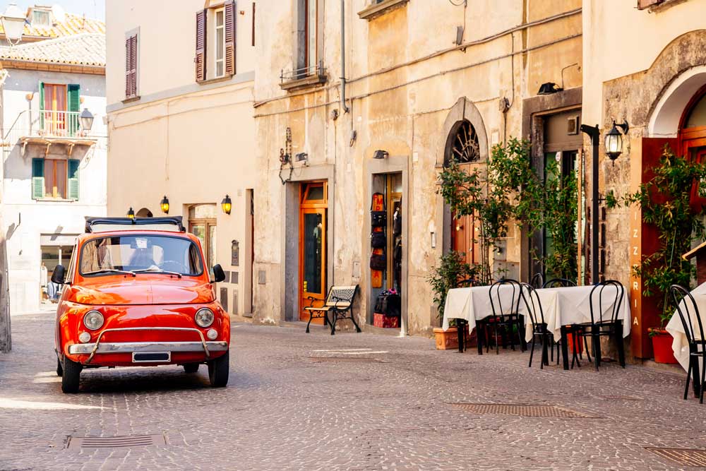 Italiensk gata med en gammaldags bil och ett fik